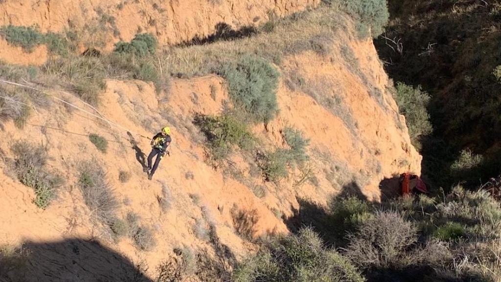 Un bombero, ayudado por cuerdas, desciende hacia el turismo accidentado.