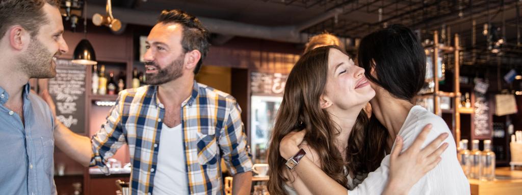 Dos mujeres se saludan con un beso y los hombres con la mano.