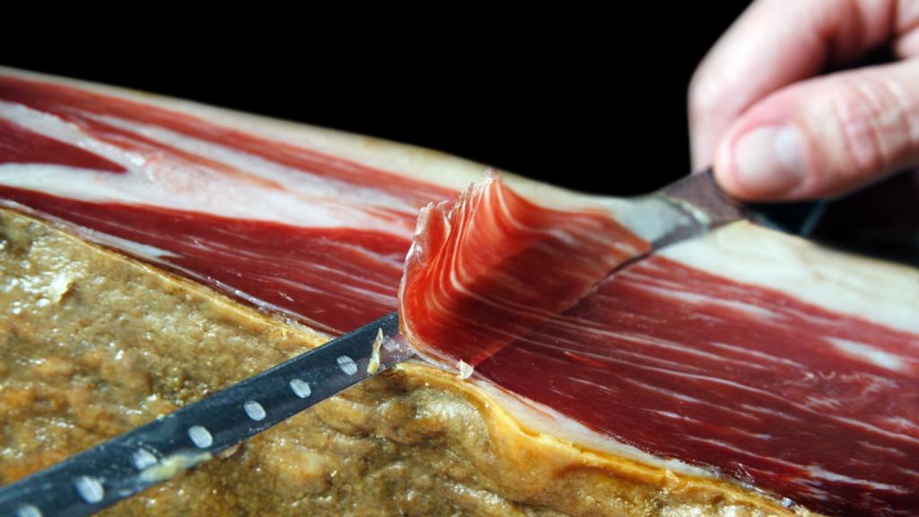 Una persona corta una fina loncha de jamón de una pata.