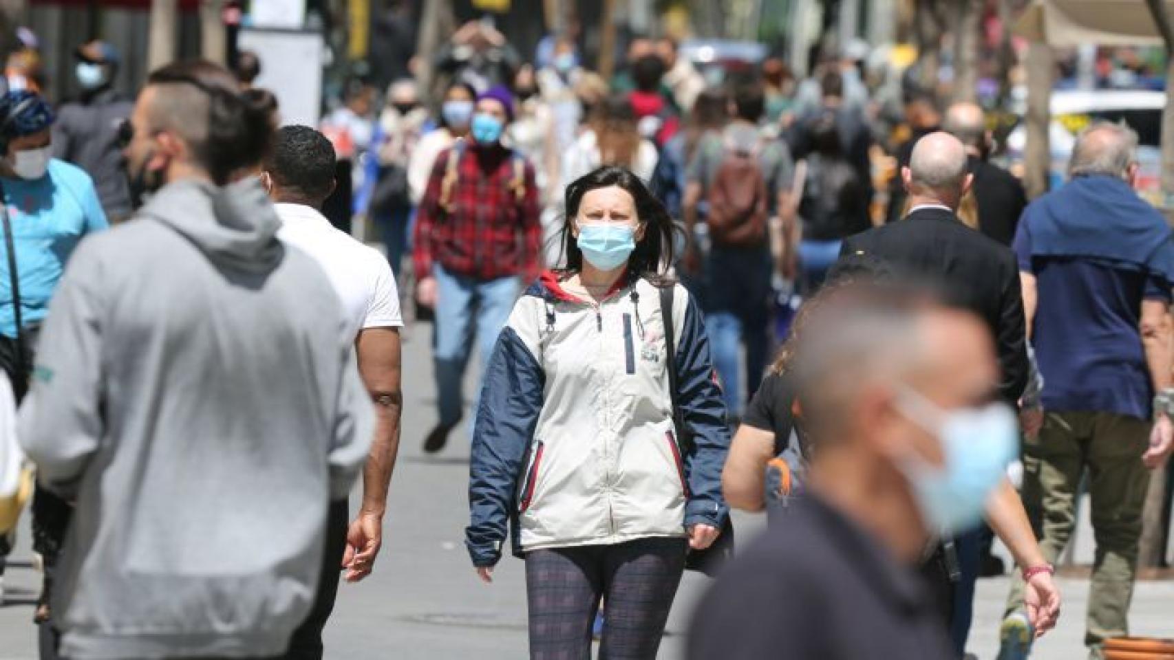 Una mujer camina por la calle con su mascarilla bien puesta.