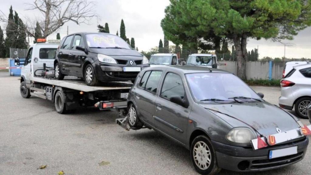Una grúa transporta a dos coches a un desguace.