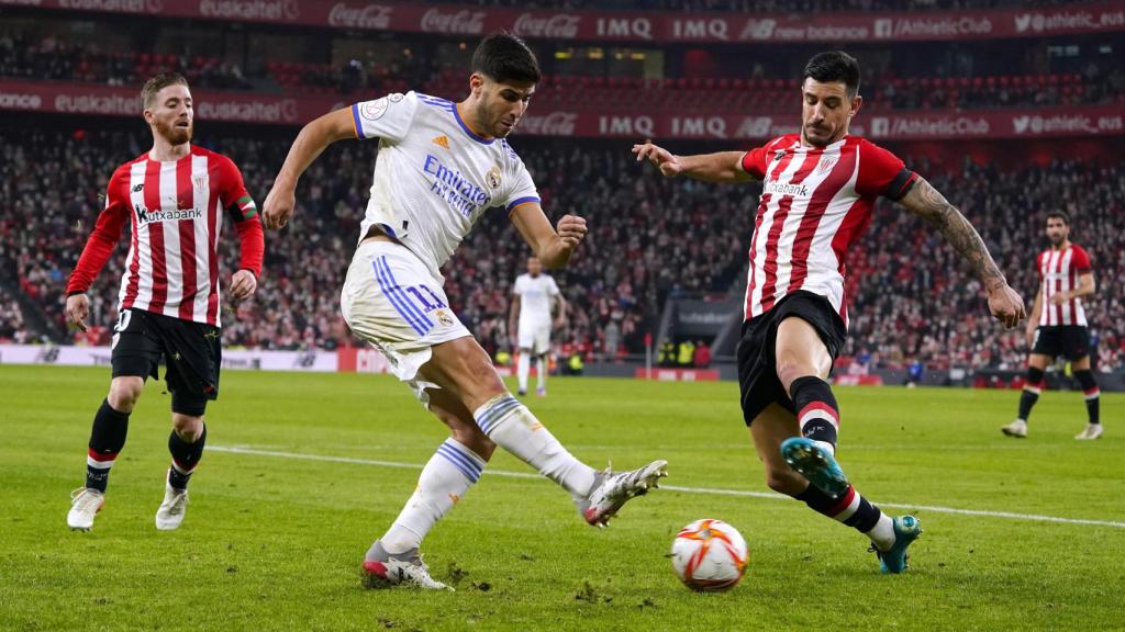 Marco Asensio centra un balón presionado por Yuri Berchiche e Iker Muniain