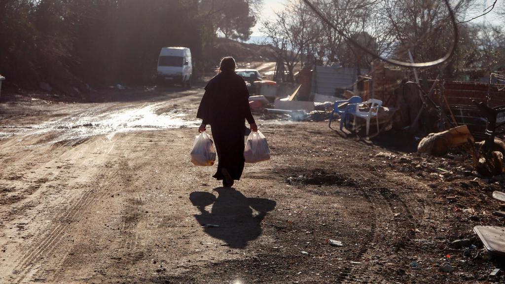 Una mujer camina con bolsas que ha recogido en la entrega de regalos y alimentos organizada por la Fundación Madrina, en la Cañada Real.