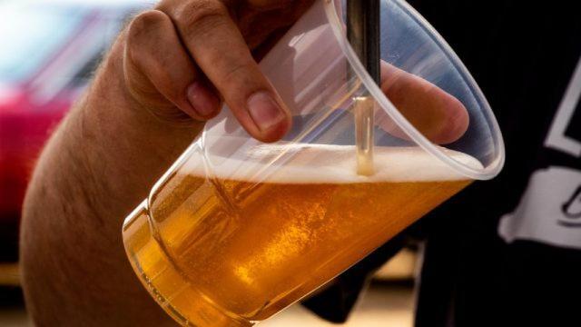 Un hombre rellena un vaso de plástico con cerveza.