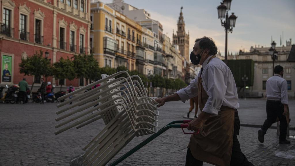 Un camarero recoge el mobiliario de un bar en Sevilla.