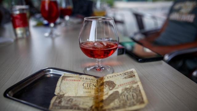 Un billete de 100 pesetas junto a una copa en la barra de un bar.