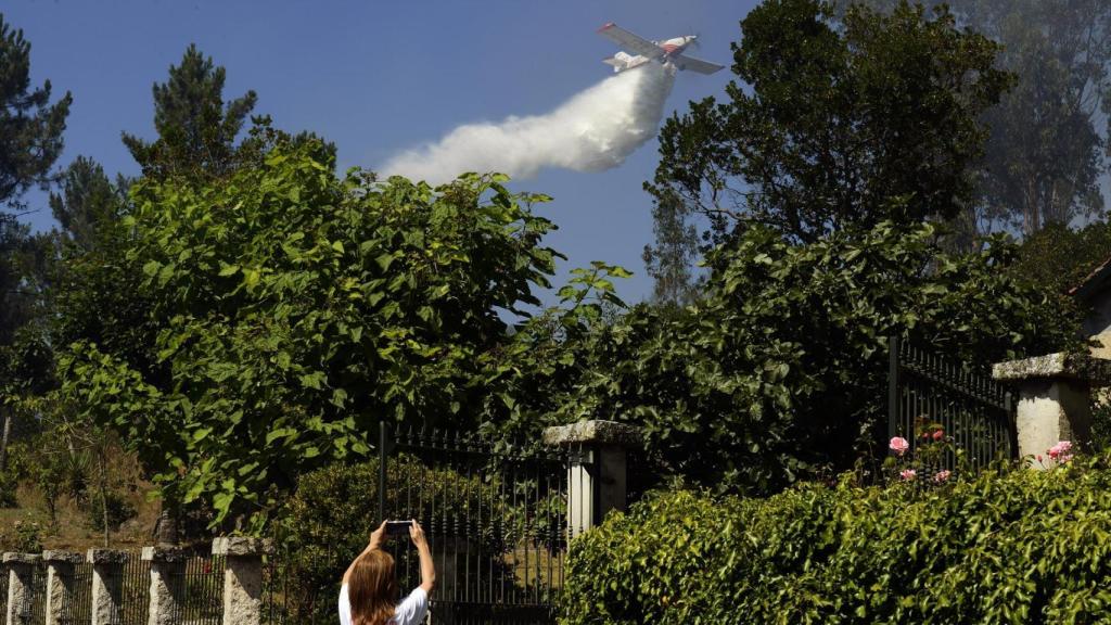 La propietaria de una finca afectada por un incendio forestal fotografía cómo un hidroavión arroja agua sobre el fuego en julio de 2021, en la parroquia de Santa Mariña do Monte, Ourense.