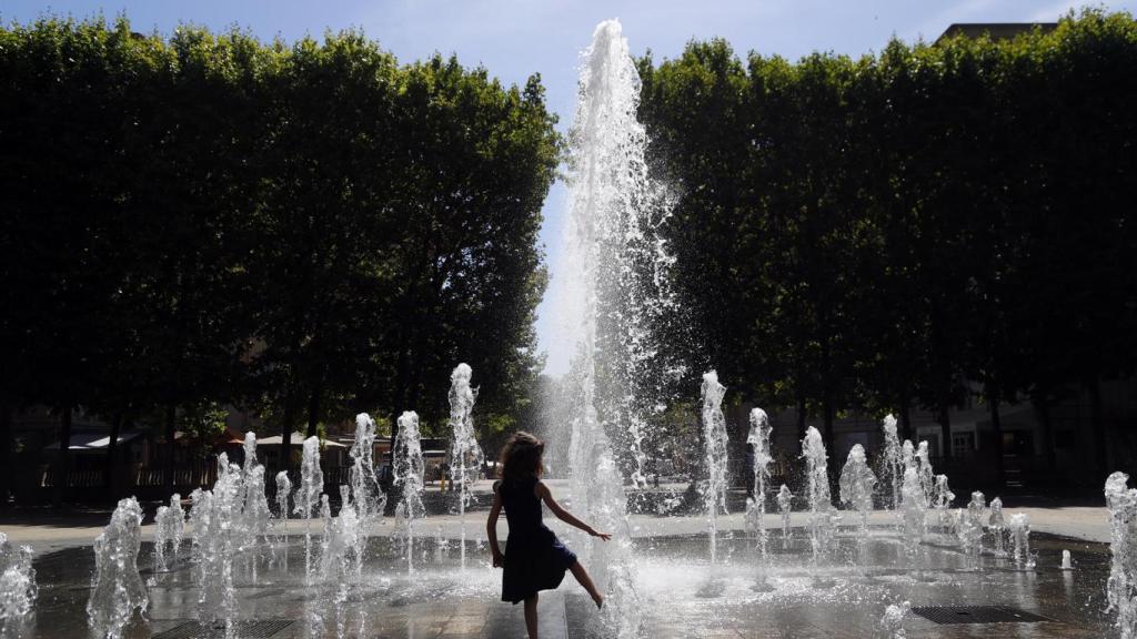 Una niña se refresca en una fuente.