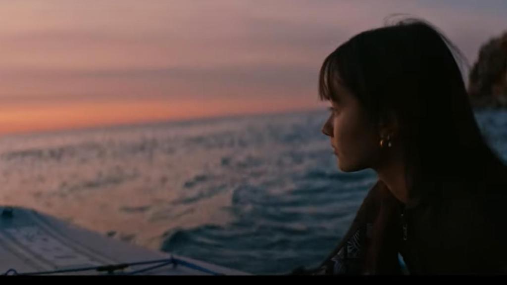 Una chica mira el atardecer en una playa valenciana con su tabla de surf.
