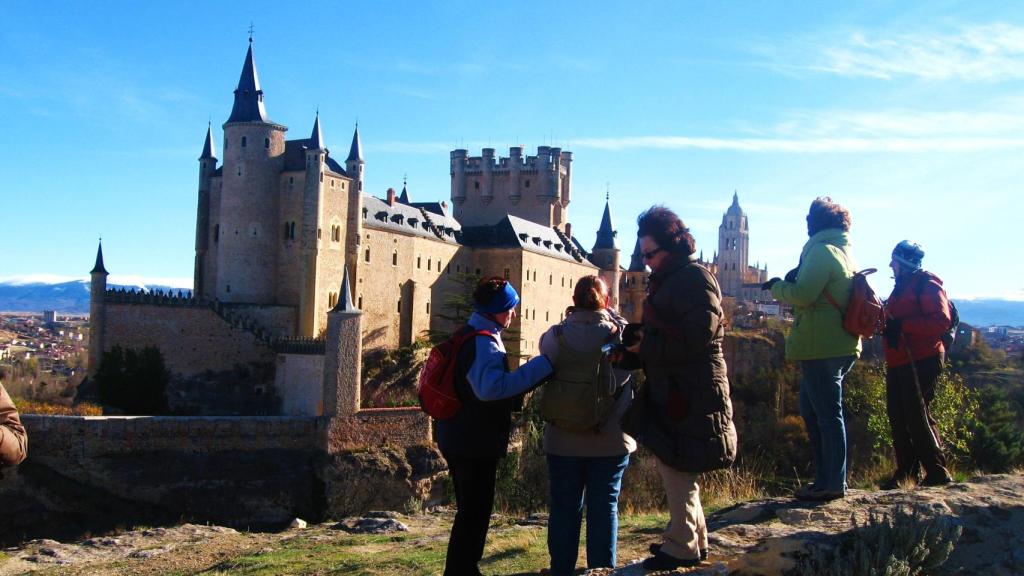 Imagen de unos viandantes en Segovia con el Alcázar al fondo