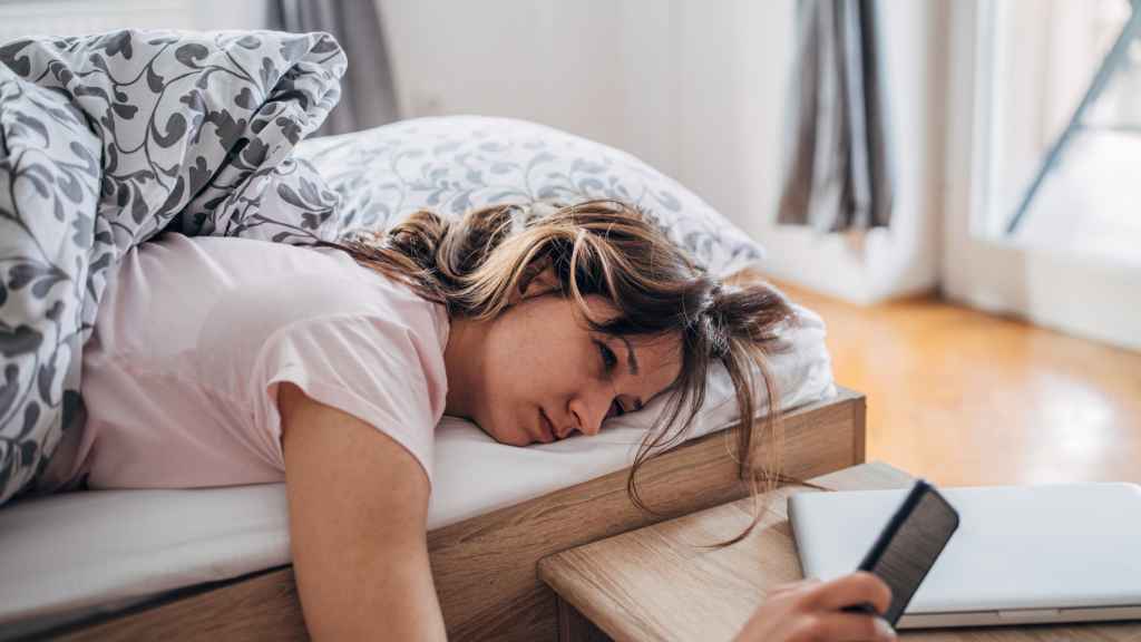 Una mujer mira el móvil desde la cama.
