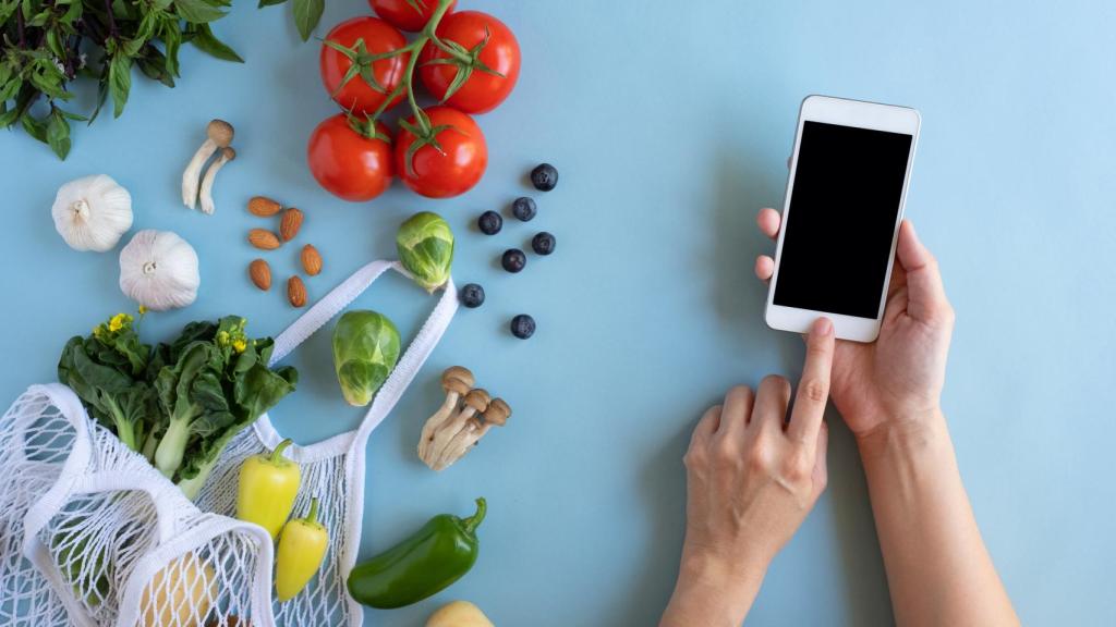 Una persona con un teléfono móvil junto a verduras y hortalizas.