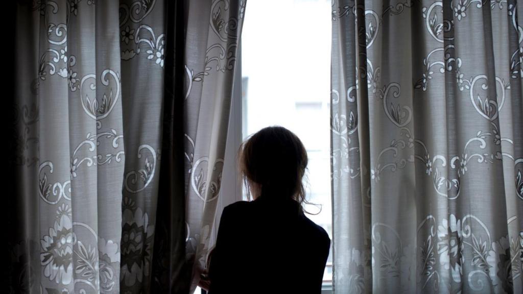 Una persona mira a través de una ventana, en imagen de archivo.