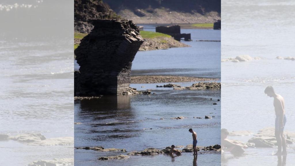 Varios jóvenes caminan por las aguas muy poco profundas del Rio Miño a su paso por Portomarín.