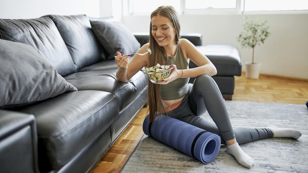 Una mujer joven come una ensalada después de haber practicado deporte.