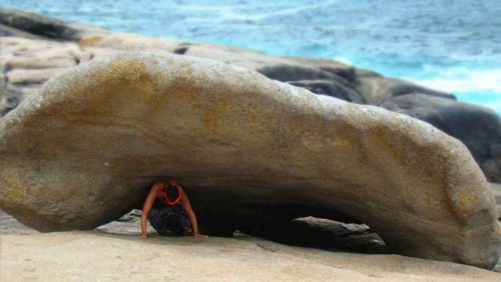 Una persona pasa bajo la Pedra dos Cadrís, en Muxía, para curar su dolor de espalda.