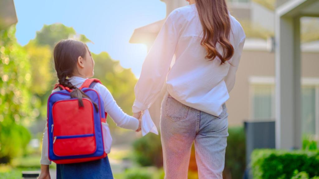 Una niña camina hacia el colegio de la mano de su madre.