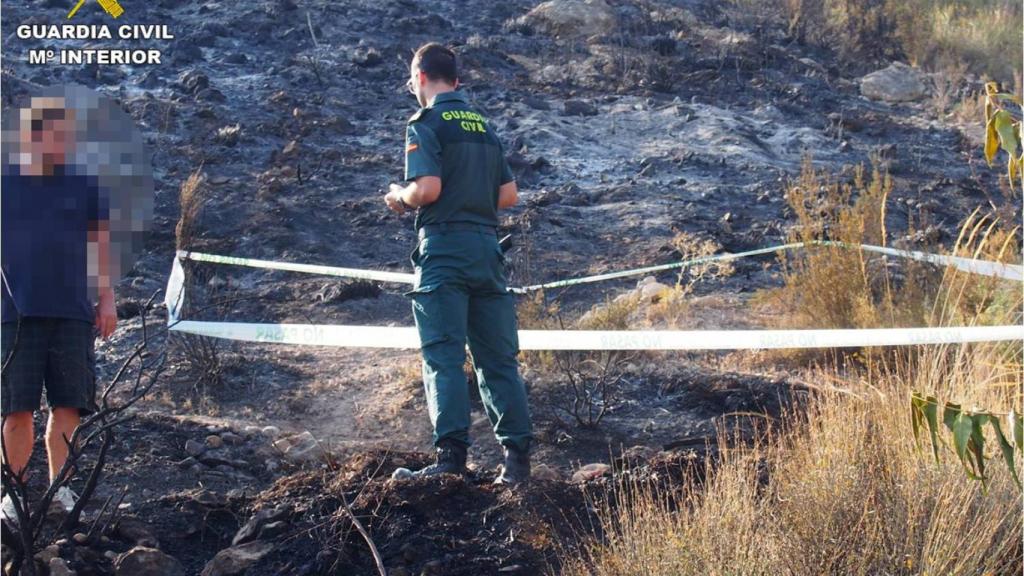 El vecino investigado con un agente de la Guardia Civil en el lugar del incendio.