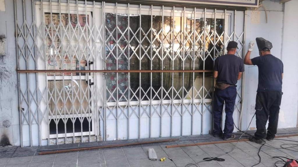 Dos operarios refuerzan el cierre exterior del local desalojado.
