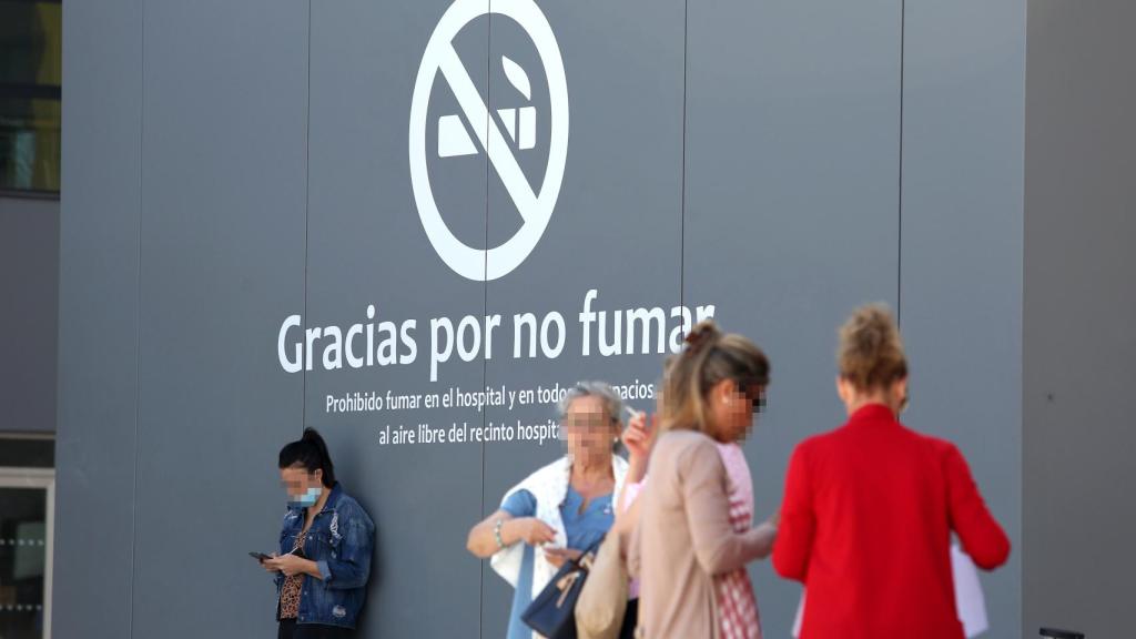 Varias personas, entre ellas una fumadora, junto a uno de los carteles.