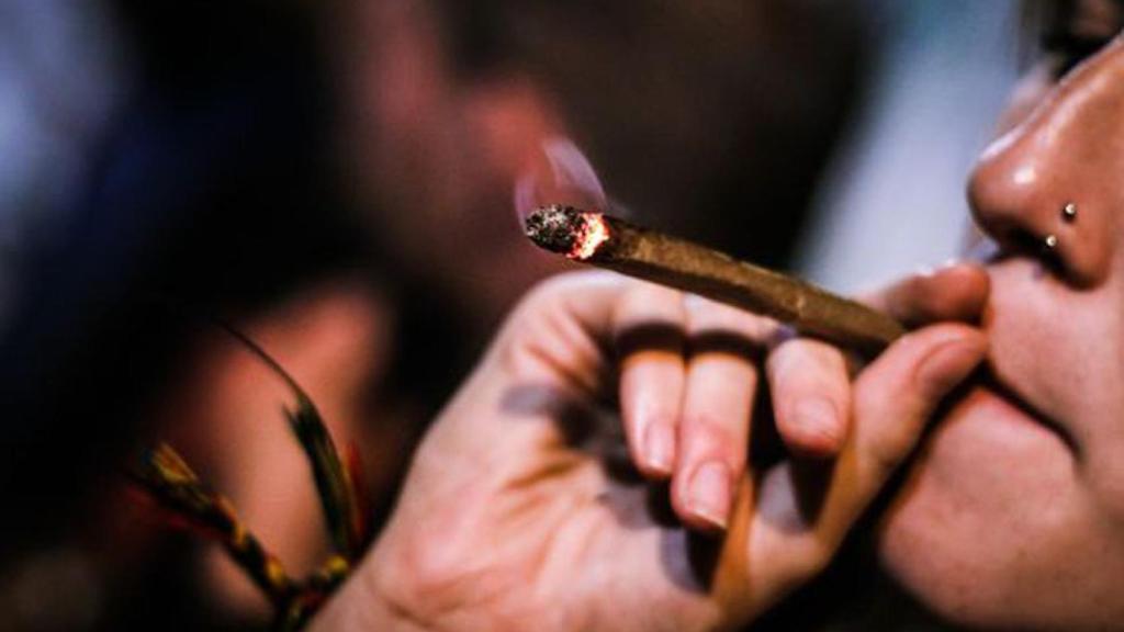 Una persona le ha una calada a un porro.