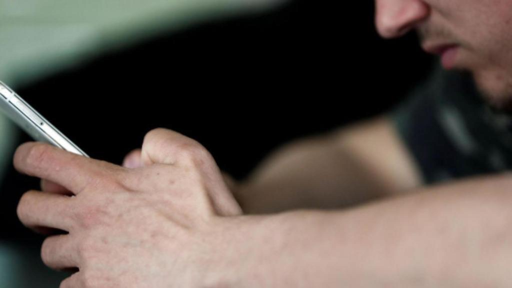 Un joven deprimido sujeta su móvil con la mano.