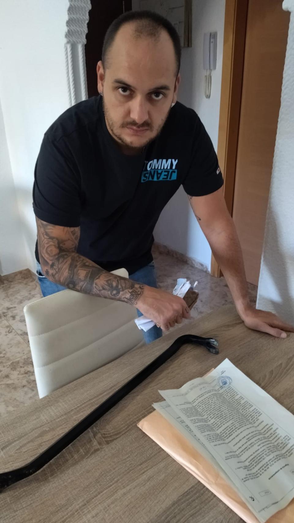 Pedro, este lunes, en su vivienda de Cartagena, mostrando la pata de cabra con la que abrió la puerta de la casa de su abuela y la denuncia que presentó en la Guardia Civil por la ocupación del inmueble.