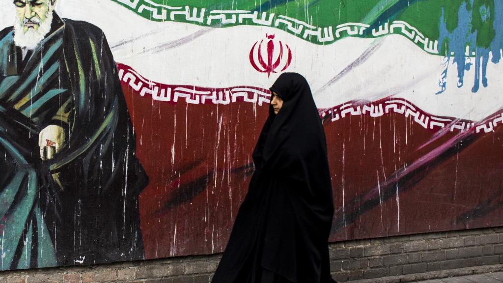 Una mujer junto a un mural con la bandera iraní y el ayatolá Ruholá Jomeini en Teherán.