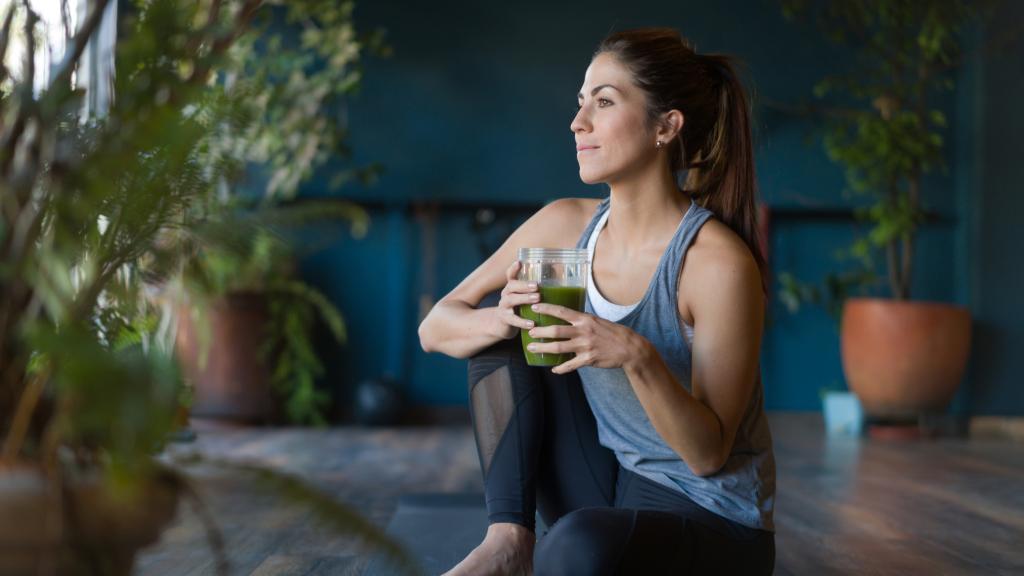 Una mujer se bebe un batido détox en el gimnasio.