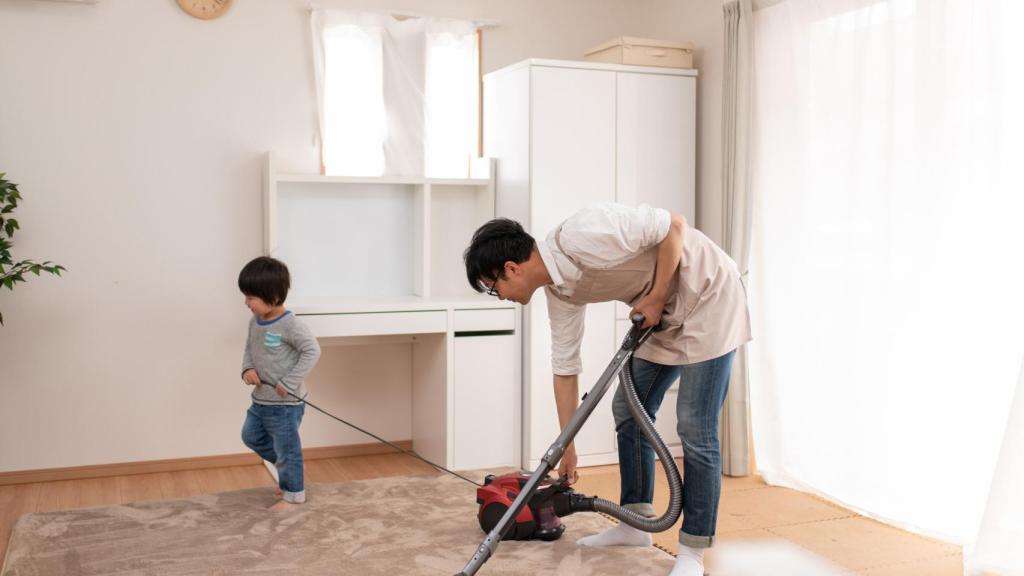 Imagen de archivo con un niño ayudando a su padre a pasar la aspiradora.