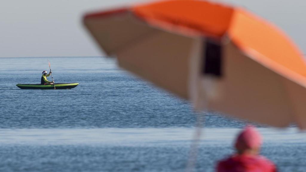 Un hombre con gorro de Papá Noel surca las aguas de la Malvarrosa en kayak durante la mañana del día de Nochebuena.