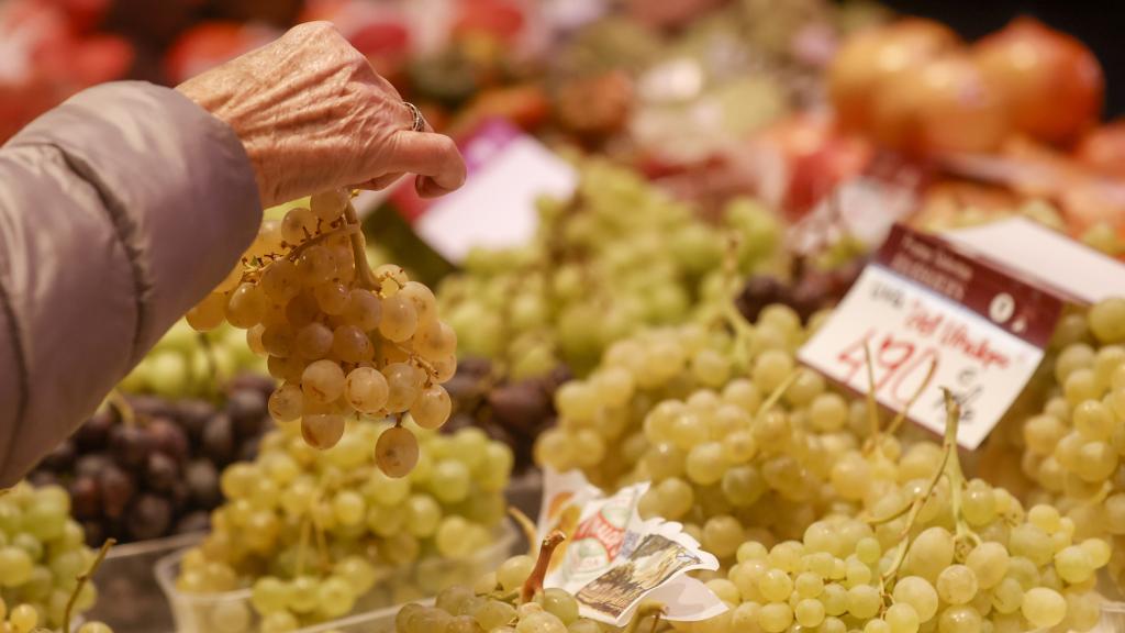 Una mujer escoge un ramillete de uvas en el mercado.