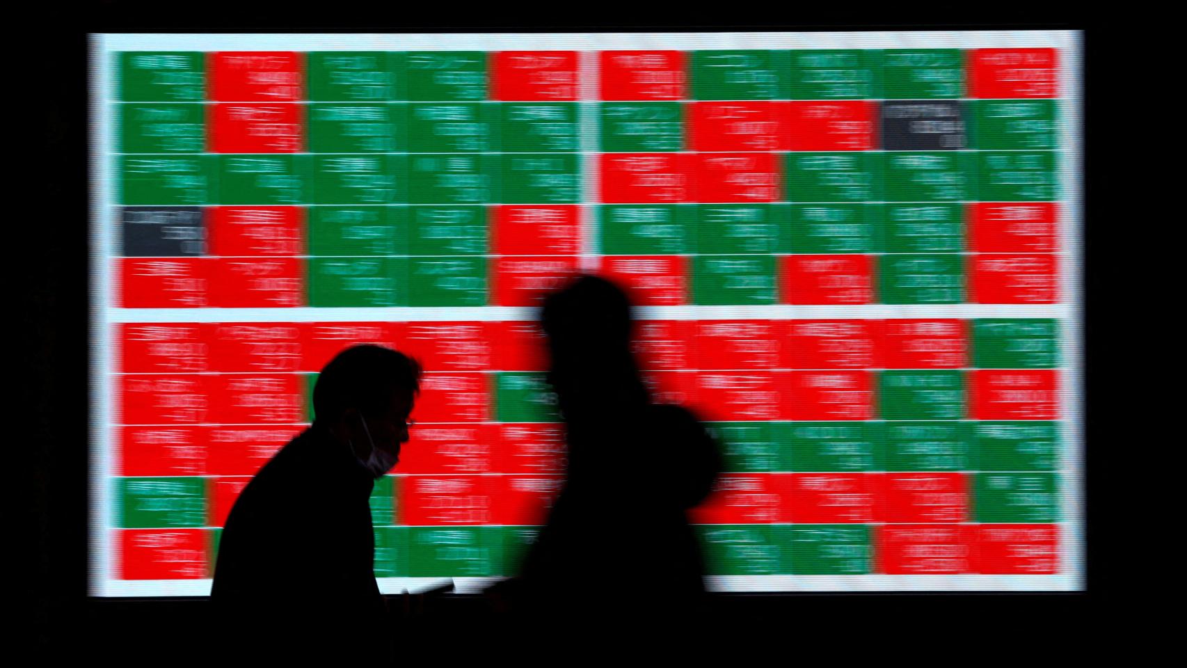 Dos personas caminan delante de un panel de cotización en el exterior de la sede de la Bolsa de Tokio.