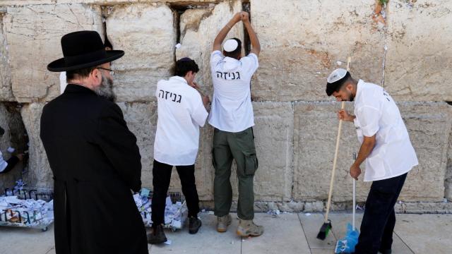 Varias personas retiran las notas del Muro de las Lamentaciones en Jerusalén.