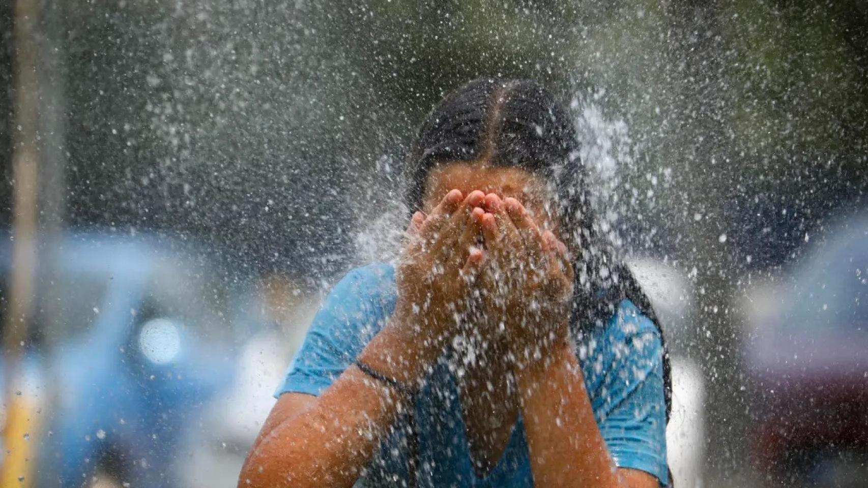 Una joven se refresca en una fuente durante una ola de calor.