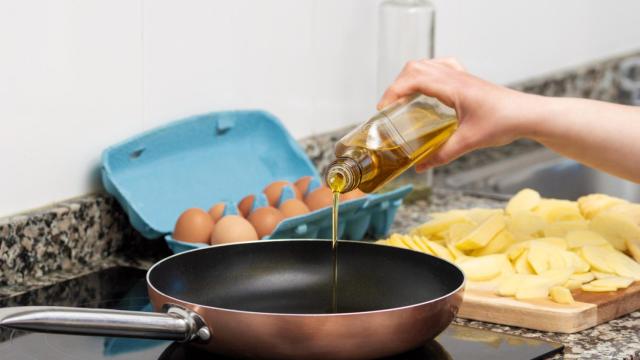 Una persona vertiendo aceite en una sartén.