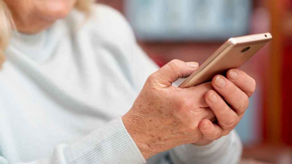 Una persona mayor haciendo uso de un teléfono móvil.