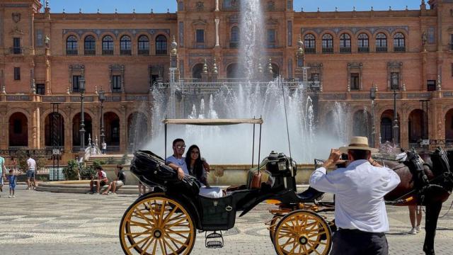 Dos turistas se hacen una foto en un coche de caballos en la Plaza de España de Sevilla.