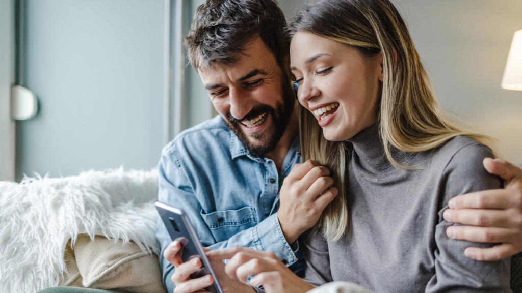 Una pareja joven se muestra feliz mirando su teléfono móvil.