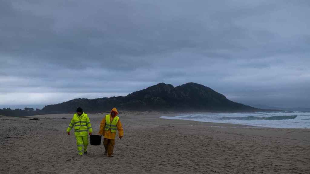 Dos hombres cargan un cubo lleno de pélets, en la playa Area Maior.