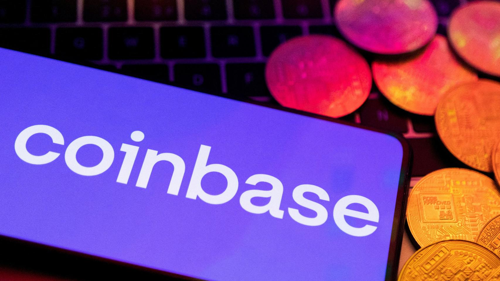 El logo de Coinbase aparece en un smartphone junto a la representación física de unas criptodivisas.