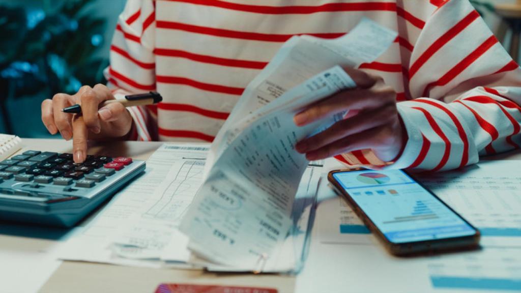 Una mujer sumando facturas con una calculadora junto a un teléfono móvil.