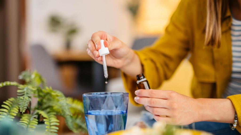 Mujer echando unas gotas de aceite esencial a un vaso de agua.