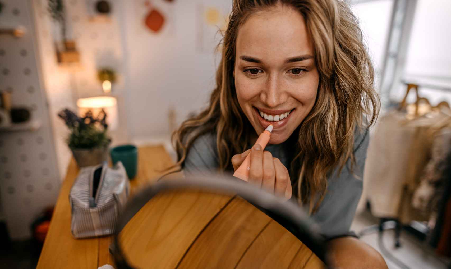 Mujer maquillándose sonriente frente a un espejo.