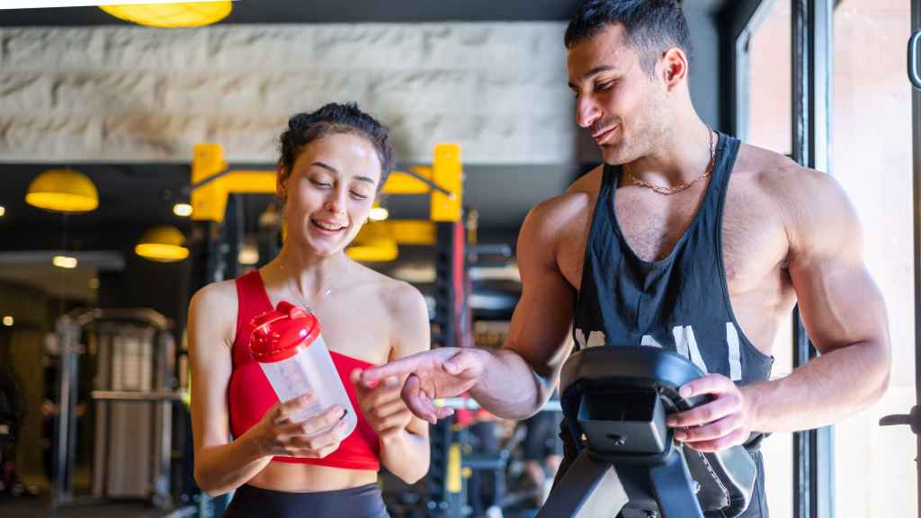Foto de archivo de una hombre y una mujer tomando suplementos en un gimnasio.