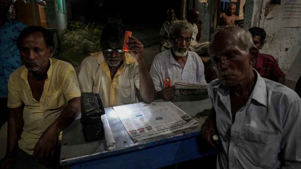 Varios residentes locales escuchan una radio durante una tarde en una zona del mercado de Ghoramara.
