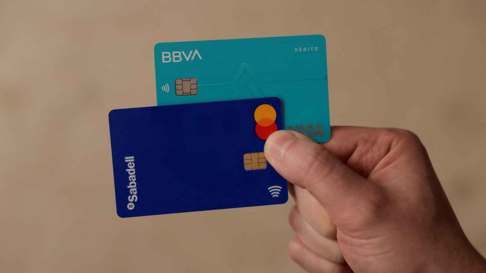 Una mano sujeta dos tarjetas de BBVA y Sabadell, respectivamente.