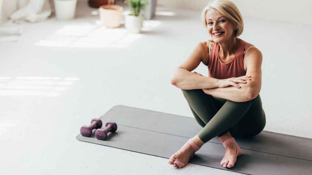 Mujer sentada sobre una esterilla con las mancuernas al lado.
