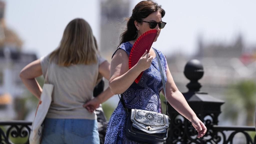 Una mujer se abanica a su paso por el Puente de Triana.