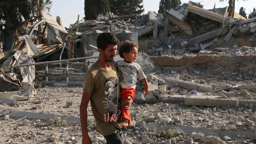 Un hombre palestino carga a un niño mientras camina cerca de los escombros, luego de un ataque israelí contra una escuela que alberga a personas desplazadas, en medio del conflicto entre Israel y Hamas, en Khan Younis, en el sur de la Franja de Gaza, el 27 de junio de 2024.